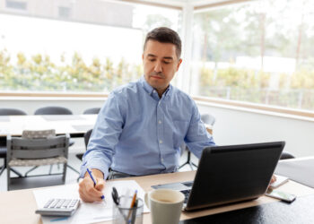 remote job, business and people concept - middle-aged man with calculator, papers and laptop computer working at home office