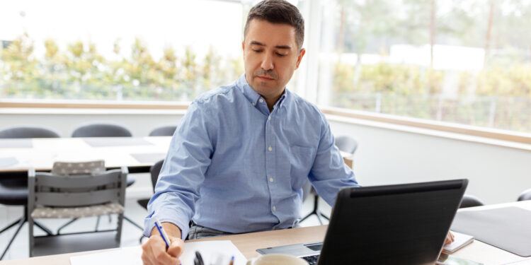 remote job, business and people concept - middle-aged man with calculator, papers and laptop computer working at home office
